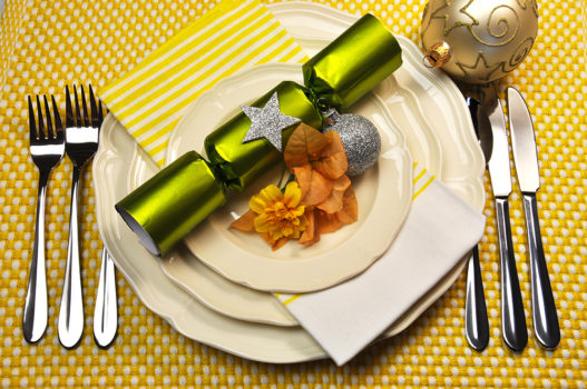 Yellow Christmas holiday table setting with plates, cutlery, baubles, Christmas cracker bon bons decorations, in a yellow theme.