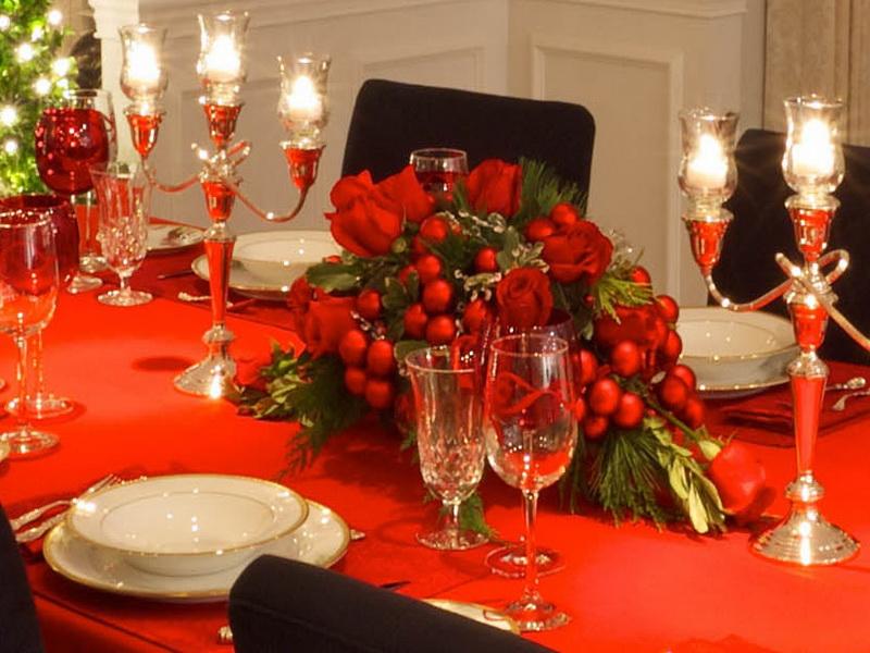 Table decorated with beautiful bright red spun polyester tablecloths and floral arrangements. Above the table can be seen beautiful candle chandeliers accompanied with other cutlery. 